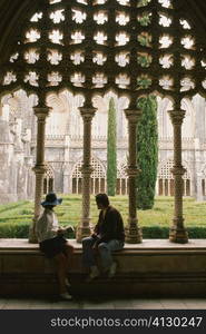 Side profile of two people sitting in the courtyard of a church, Portugal