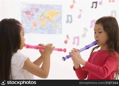 Side profile of two schoolgirls playing flutes in a classroom