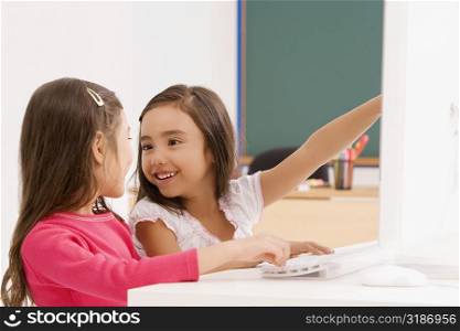 Side profile of two schoolgirls smiling in front of a computer