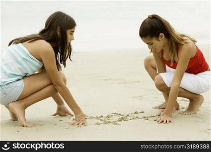 Side profile of two teenage girls drawing on sand on the beach