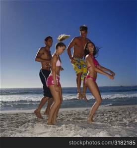 Side profile of two young couples jumping on the beach