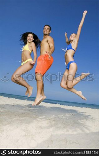 Side profile of two young women and a young man jumping on the beach