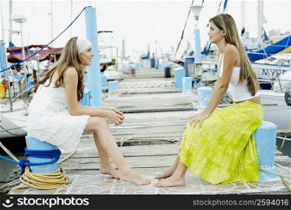 Side profile of two young women sitting at a dock and looking at each other