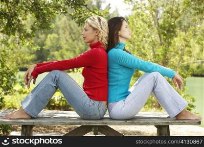 Side profile of two young women sitting back to back