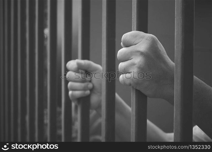 Side view and selective focus at left man's hand holding iron bars in black and white style, dramatic border fence or prison with immigrant and refugee crisis, hope to be free concept