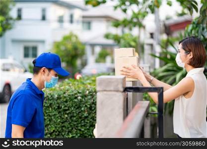 Side view asian woman with face mask customer take shopping packages from the fence post that delivery man put them on for contactless delivery. This can reduce coronavirus COVID-19 spreading.