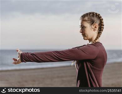 side view athletic woman stretching by beach 3