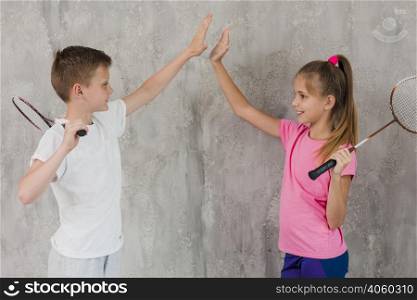 side view boy girl holding racket hand giving high five standing against wall