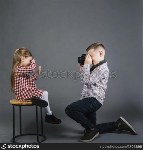 side view boy taking girl sitting stool with camera