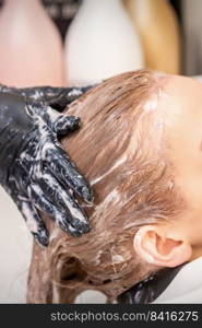 Side view close up of beautiful young caucasian woman receiving hair wash by hands of hairstylist in hair salon. Young woman receiving hair wash