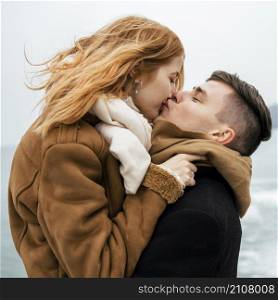 side view couple by lake during winter kissing
