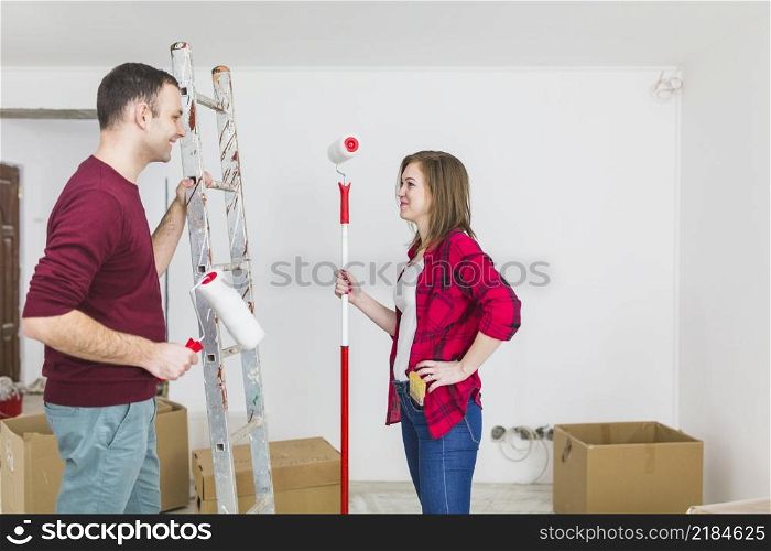 side view couple with paint rollers ladder