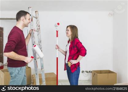 side view couple with paint rollers ladder