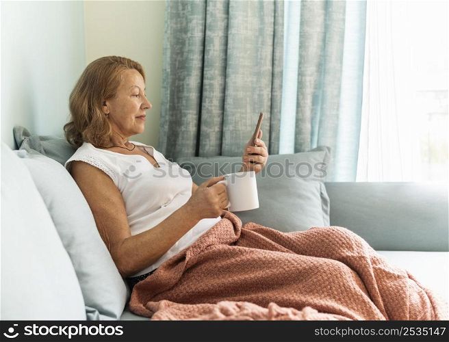 side view elder woman home during pandemic enjoying cup coffee using smartphone