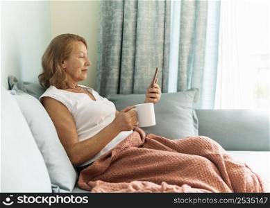 side view elder woman home during pandemic enjoying cup coffee using smartphone