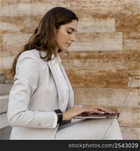 side view elegant businesswoman with smartwatch working laptop outdoors