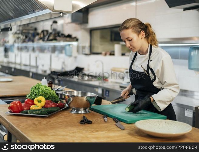 side view female chef kitchen slicing vegetables
