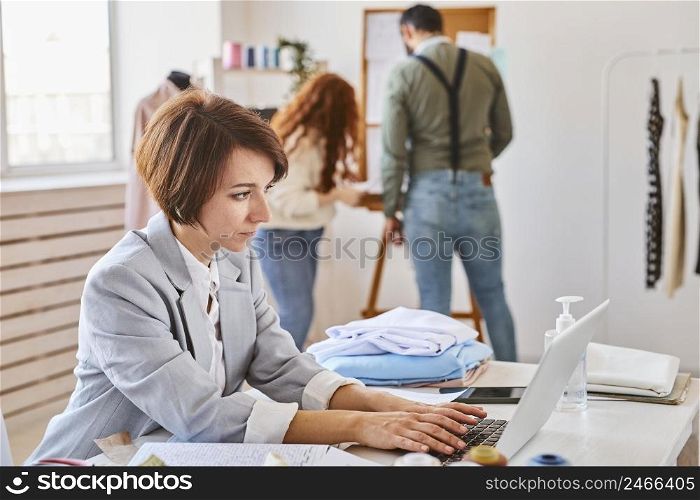 side view female fashion designer working atelier with laptop colleagues