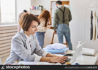 side view female fashion designer working atelier with laptop colleagues