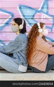 side view female friends with face masks outdoors listening music headphones