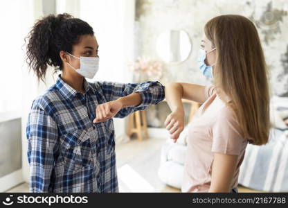 side view female friends with medical masks practicing elbow salute