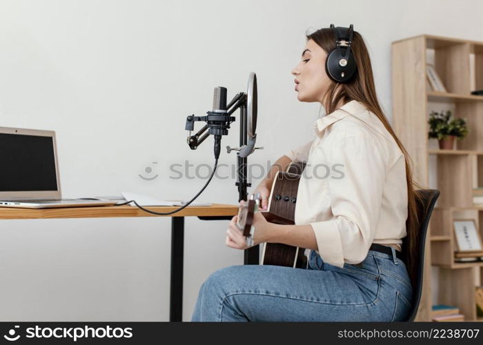 side view female musician recording song with microphone while playing acoustic guitar home