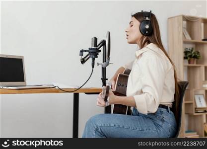 side view female musician recording song with microphone while playing acoustic guitar home