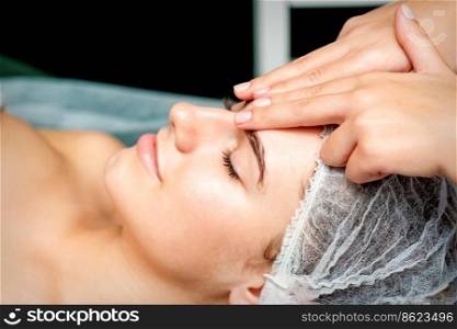 Side view fingers of female therapist making anti-age massage of forehead wrinkles to young caucasian woman in spa beauty salon. Female therapist making forehead massage