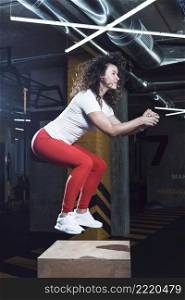 side view fit woman doing jumping squat wooden box