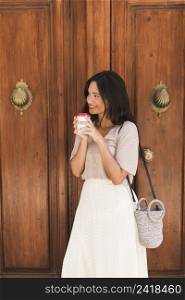 side view girl standing front door holding disposable coffee cup