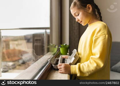 side view little girl holding planted seeds egg carton