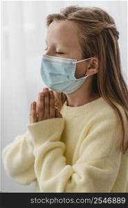 side view little girl praying with medical mask