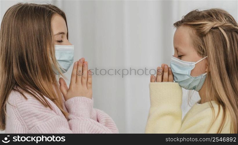 side view little girls praying with medical masks