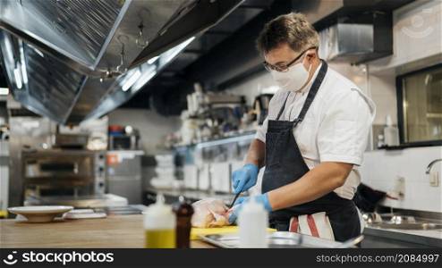 side view male chef with mask cutting chicken