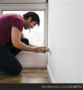 side view male electrician carrying tester mouth while fixing plug socket home