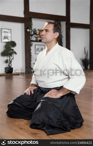side view male martial arts instructor sitting practice hall