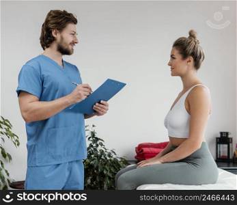 side view male osteopathic therapist with female patient signing clipboard clinic