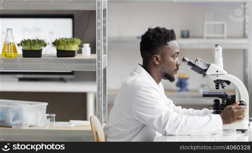 side view male researcher laboratory looking through microscope