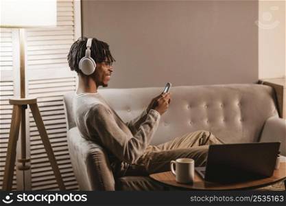 side view man home couch using smartphone headphones