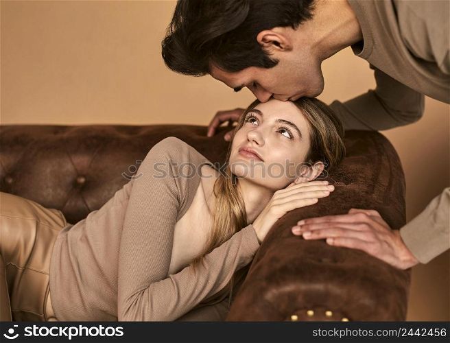 side view man kissing woman forehead while she sits sofa
