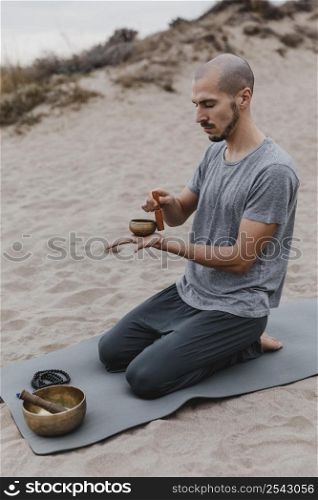 side view man mat outdoors with singing bowl