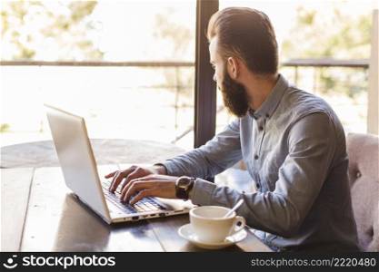 side view man typing laptop keypad with cup coffee desk