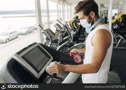 side view man with medical mask disinfecting treadmill gym