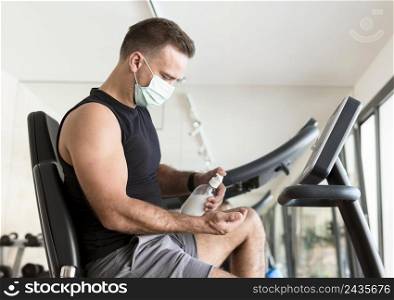 side view man with medical mask using hand sanitizer gym