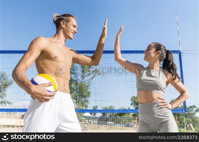 side view man woman high fiving each other while playing volleyball