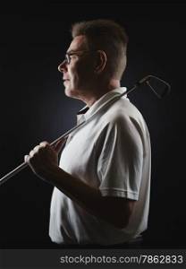 Side view, mature man golfer wearing a white shirt and he holds a iron golf club on his shoulder - studio shot, black background