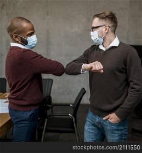 side view men elbow saluting each other during meeting wearing medical masks