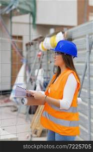 Side view of a beautiful young architecture student wearing safety gear holding blueprints and checking a construction site. Work and apprenticeship concept.. Architecture student holding blueprints checks a construction site