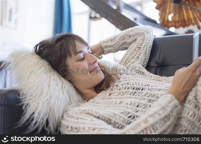 side view of a beautiful young smiling woman lying on leather couch relaxing while using a mobile phone at home. Rafa Fernandez