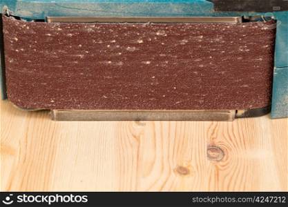 Side view of a belt sander on pine floor or table sanding surface
